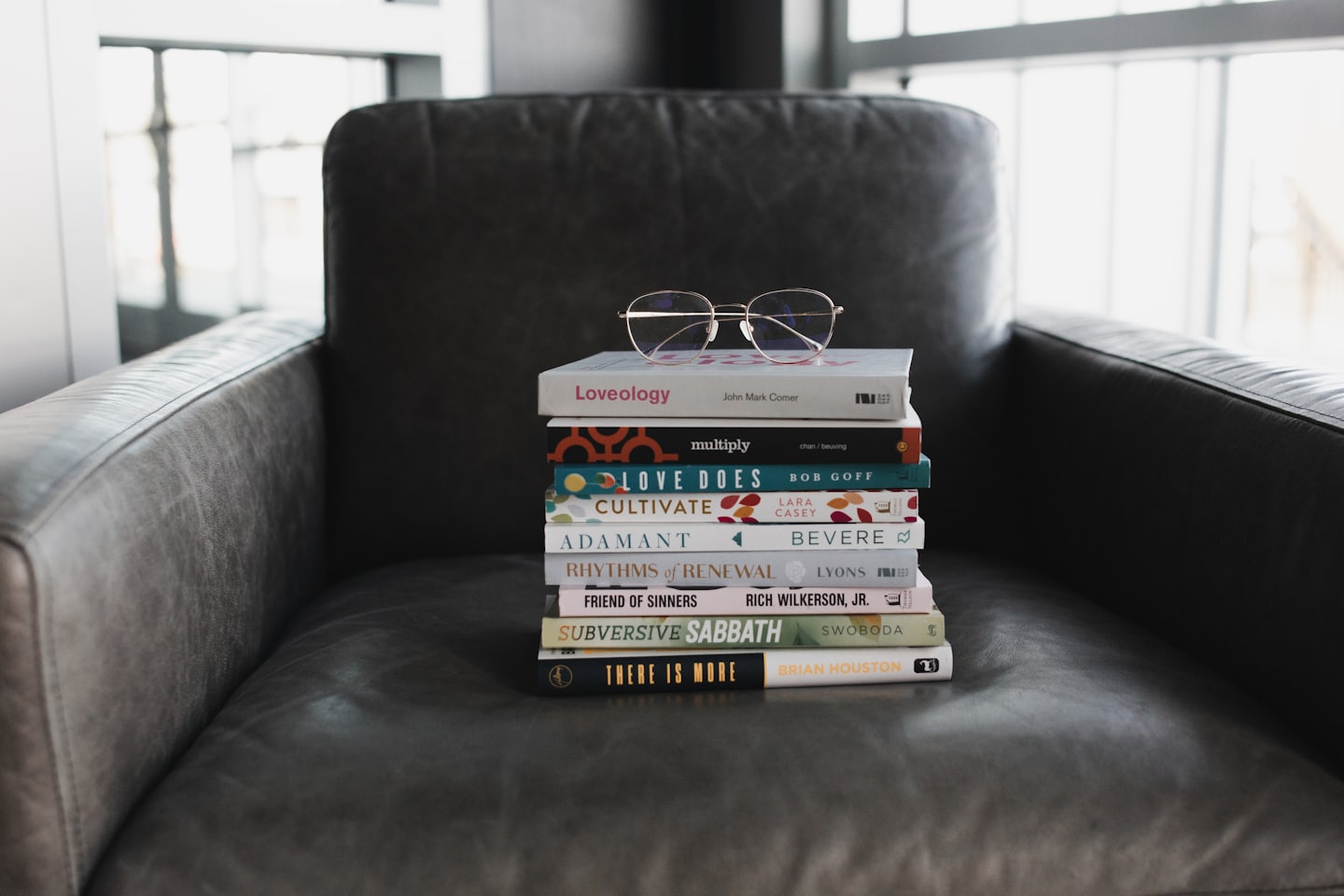 Gold-rimmed reading glasses on a stack of books on a leather armchair.
